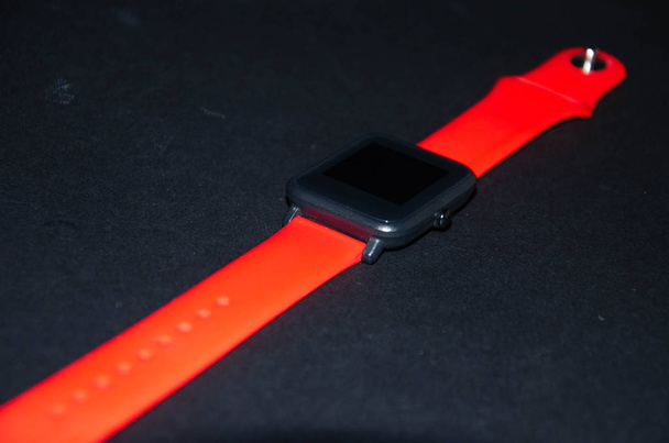 Smart Watch mit rotem Armband. Smartwatch mit einem hellen Armband an der Hand und auf schwarzem Hintergrund. Nachverfolgung sportlicher Aktivitäten. Sport treiben - Foto, Bild