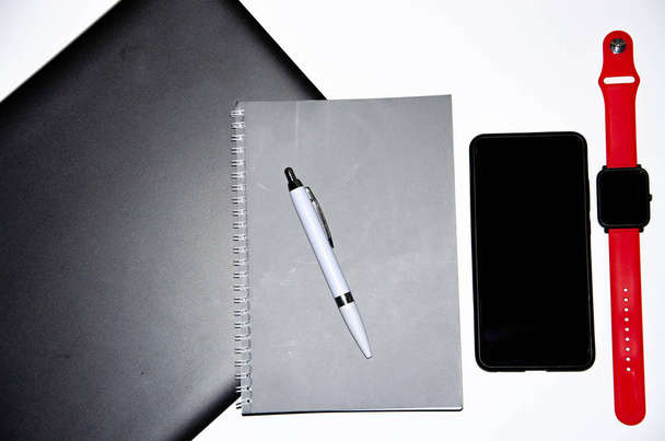 白と黒の背景にペンでノートパソコン、スマートフォン、スマートウォッチとノートブック。作曲。異なる側面からの眺め。ペーストをコピーし、平らな樹皮。機能とデザインのためのツール。フリーランサー職場 - 写真・画像