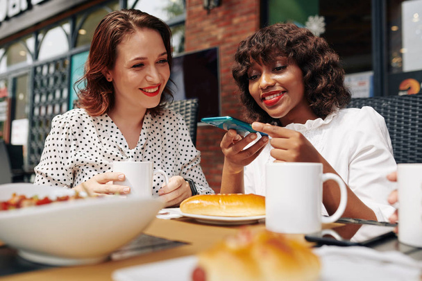 Веселі багатоетнічні друзі-жінки фотографують їжу, коли обідають в кафе разом
 - Фото, зображення
