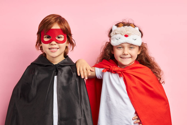 Positive two children in cloaks and mask isolated over pink background - Foto, Imagen