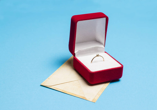 ring in een doos met een envelop op een blauwe achtergrond - Foto, afbeelding