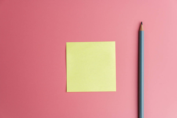 one yellow sticky note reminder and a pencil on a red background - Photo, Image