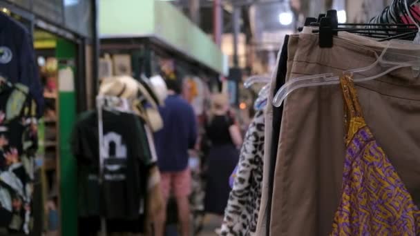Stojak na ubrania w sklepie z używanymi rzeczami i zdezorientowani ludzie na tle - Materiał filmowy, wideo