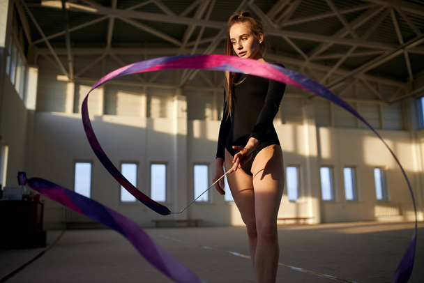Young gymnast girl training in dark studio - Фото, изображение