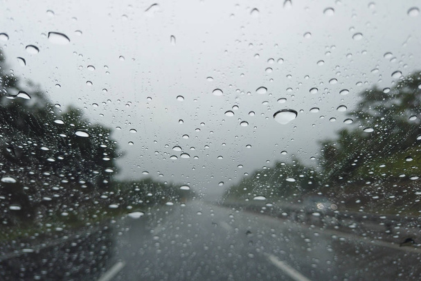 雨が車のフロントガラスに落ち、大雨の中で街の路上で車を運転 - 写真・画像