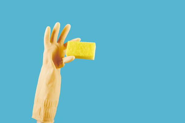 Домохозяйка в жёлтой резиновой перчатке держит кухонное мыло, изолированное на голубом
 - Фото, изображение