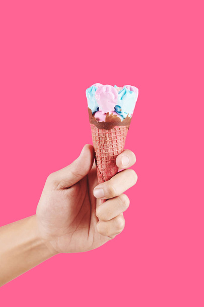 Hand with soft bubble gum taste ice-cream in waffle cone on hot pink background - Photo, Image