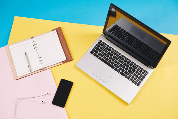 Geopend laptop, planner en smartphone met oordopjes op kleurrijk bureau van creatieve persoon, van bovenaf bekijken - Foto, afbeelding