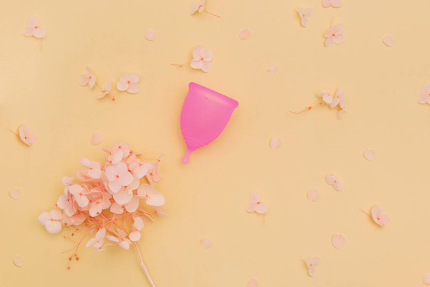 Εμμηνορροϊκό κύπελλο με λουλούδια ορτανσία σε παστέλ πορτοκαλί φόντο. - Φωτογραφία, εικόνα