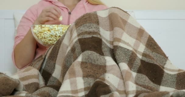 Μια γυναίκα βλέπει ταινία ξαπλωμένη στο κρεβάτι και τρώει ποπ κορν - Πλάνα, βίντεο