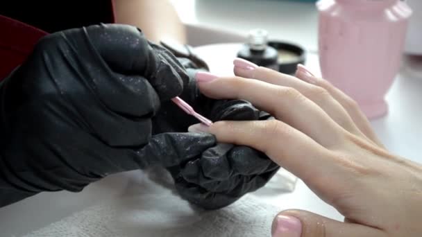 Μανικιούρ master σε μαύρα γάντια εφαρμόζει ροζ βερνίκι νυχιών στα νύχια - Πλάνα, βίντεο