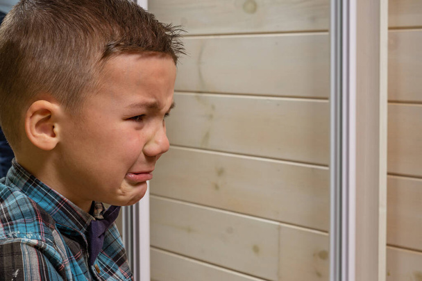 Un garçon de 4 ans dans une chemise de bureau bleue pleure sur un fond de bois clair
. - Photo, image