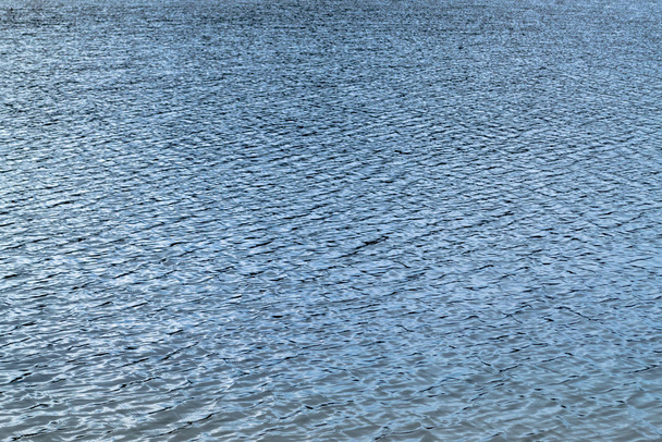 Niebieska powierzchnia wody pokryta małymi falami. Jezioro lub rzeka, z opalizującą błyszczącą powierzchnią. Kontrastowe tło lub tekstura. - Zdjęcie, obraz
