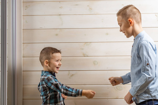 Um menino de 4 anos de idade em uma camisa azul klepy chora em um fundo de madeira leve e seu irmão, 10 anos, está de pé
. - Foto, Imagem
