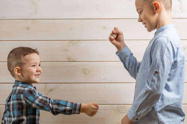 4-letni chłopiec w niebieskiej koszuli klepsydry płacze na jasnym drewnianym tle, a jego brat, 10 lat, stoi. - Zdjęcie, obraz