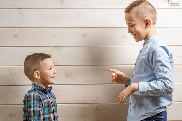 A 4-year-old boy in a blue klepy shirt cries on a light wooden background and his brother, 10 years old, is standing. - Photo, image
