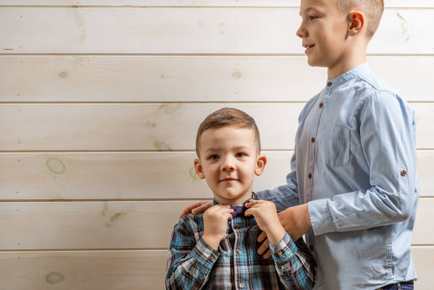 Un niño de 4 años de edad, vestido con una blusa azul, llora sobre un fondo de madera clara y su hermano, de 10 años, está de pie.
. - Foto, Imagen
