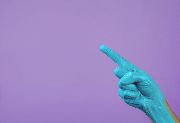 χέρι σε μπλε χρώμα σε μωβ φόντο, το δάχτυλο δείχνει να αντιγράψετε χώρο - Φωτογραφία, εικόνα