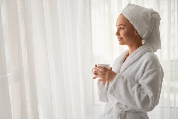 Girl in bathrobe holding cup with coffee. - 写真・画像