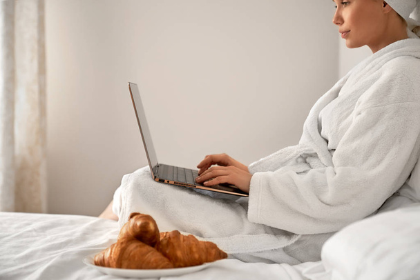 Woman in bathrobe typing on laptop. - Foto, Imagen