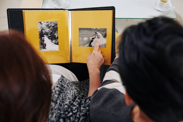 Μητέρα που δείχνει τις ασπρόμαυρες φωτογραφίες του γάμου της στον ενήλικο γιο της, θέα από ψηλά - Φωτογραφία, εικόνα