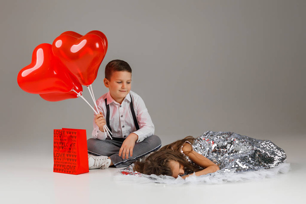 child boy holds red heart shaped balloons and girl lies nearby - Foto, afbeelding