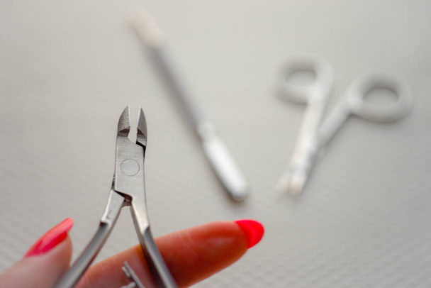 Tesoura de cutícula de garras em dedos femininos, tesoura e lâmina de cutícula no fundo embaçado
. - Foto, Imagem