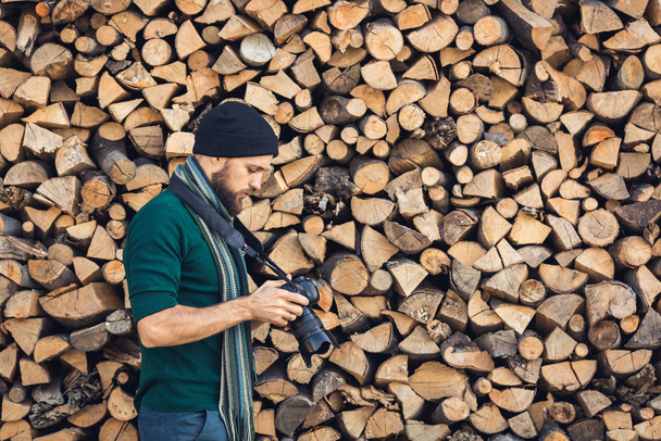 bebaarde fotograaf in de natuur met digitale camera op brandhout muur achtergrond. - Foto, afbeelding