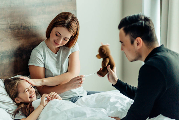 joyful father and mother with ill daughter on bed - Foto, afbeelding
