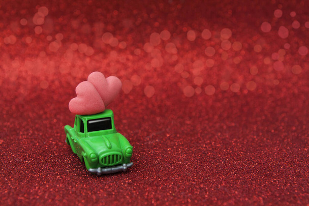 Hračkové auto se dvěma srdci na červeném třpytivém pozadí. Kopírovat prostor  - Fotografie, Obrázek