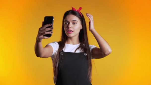 Smiling happy girl making selfie on smartphone over yellow background. Technology, mobile device, social networks concept. - Video, Çekim