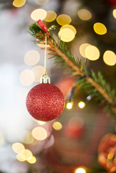 Red ball on a Christmas tree. Christmas glass toy on bokeh background with garlands. - Photo, Image