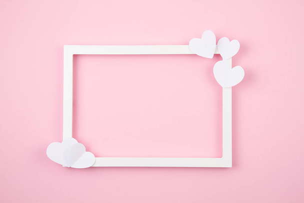Corazones de papel y marco blanco sobre el fondo rosa pastel. Amor, San Valentín, día de la madre, tarjetas de felicitación de cumpleaños, invitación, concepto de celebración
 - Foto, Imagen
