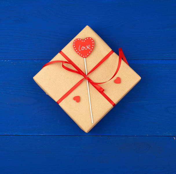 Подарок, завернутый в коричневую крафтовую бумагу и завязанный тонкой красной лентой
 - Фото, изображение