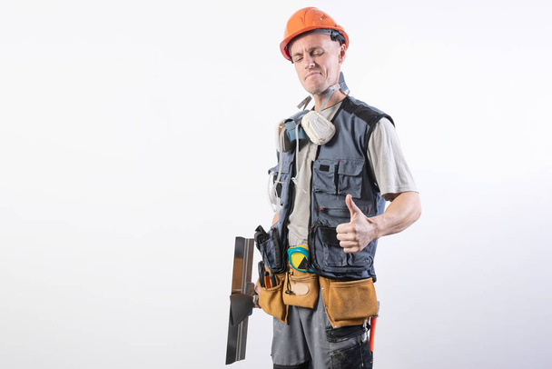 Builder with a spatula. And showing thumbs up. In work clothes and hard hat. On a light gray background. - Photo, Image