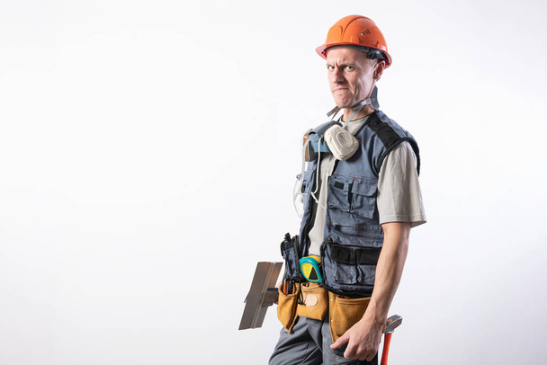 Builder with a spatula. With a funny face. In work clothes and hard hat. On a light gray background. - Photo, Image