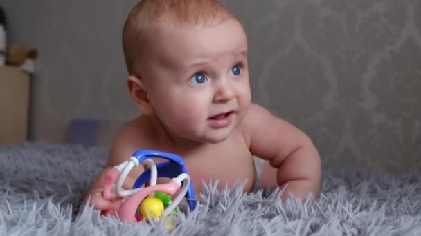 entzückende Grimasse lustiges Baby in einer Windel auf allen Vieren, auf einem Karo stehend, blickt auf einen grauen Hintergrund. - Filmmaterial, Video