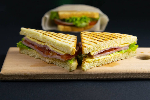 Сэндвич из нескольких ломтиков белого хлеба на деревянной доске. Наполнитель сэндвича состоит из сыра и ветчины
 - Фото, изображение