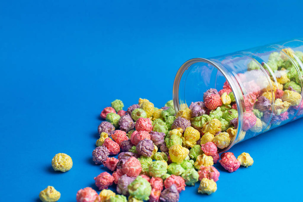 Mnohobarevné ovoce ochucené popcorn ve skleněných pohárech na modrém pozadí. Kukuřice obalená cukrem. - Fotografie, Obrázek