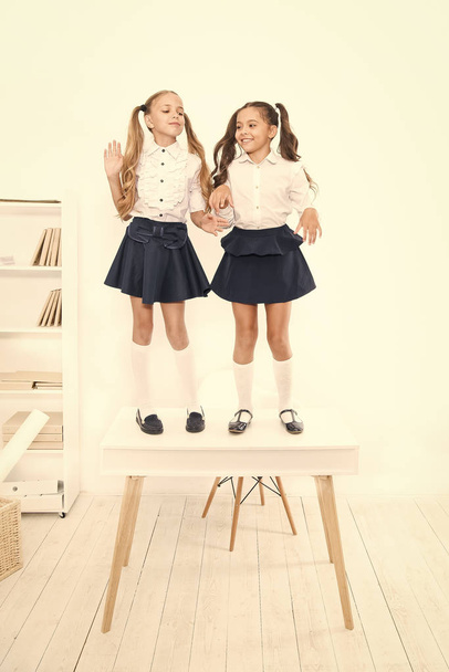 Smarty girls. Little school girls standing on desk in classroom. Small girls with long hair tails wearing fashion school style. Adorable baby girls enjoying school break - Photo, image