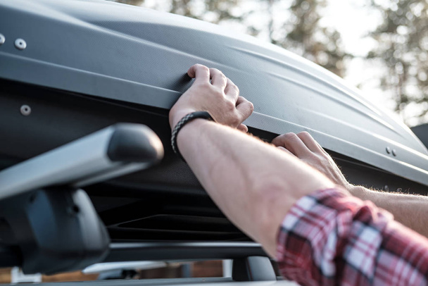 Dłonie obejmują zmontowane, pojemne bagażniki lub skrzynki ładunkowe na dachu samochodu, przed wyjazdem na rodzinne wakacje. - Zdjęcie, obraz