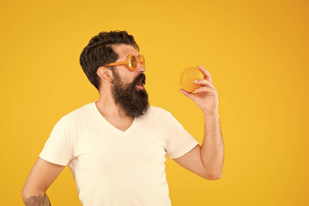Healthy food taste better. Surprised hipster looking at healthy orange fruit on yellow background. Bearded man with healthy vitamin snack. Eat healthy, be nutrition wealthy - Foto, imagen