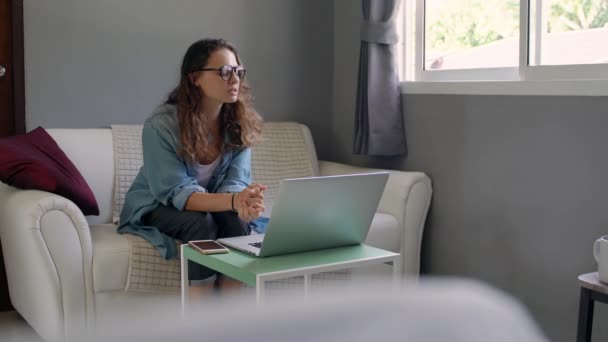 A young woman with a laptop sitting on a sofa and holds an online consultation. - Video, Çekim