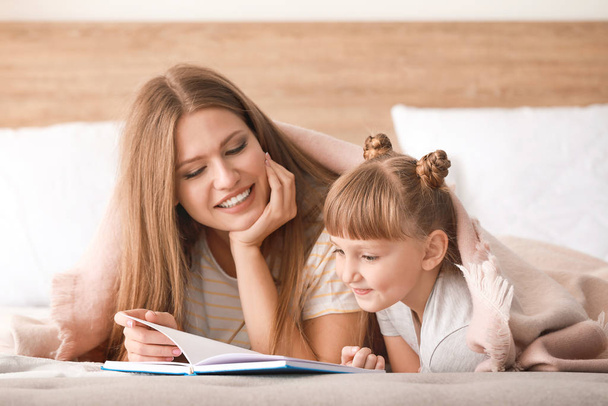 Kaunis nuori nainen ja hänen pieni tyttärensä lukevat kirjaa kotona
 - Valokuva, kuva