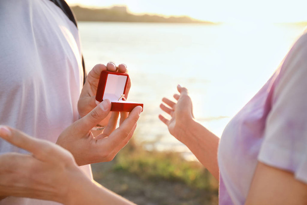 Young man proposing to his beloved near river, closeup - Foto, afbeelding