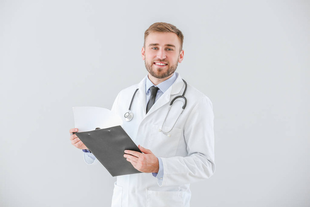 Portrait of male doctor with clipboard on light background - Fotoğraf, Görsel