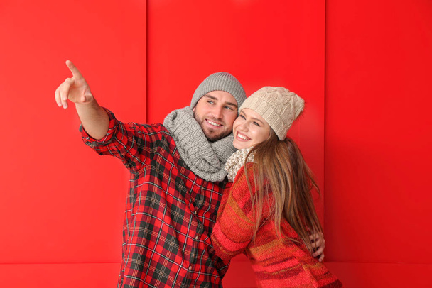 Portrait of happy couple in winter clothes showing something on color background - Photo, image