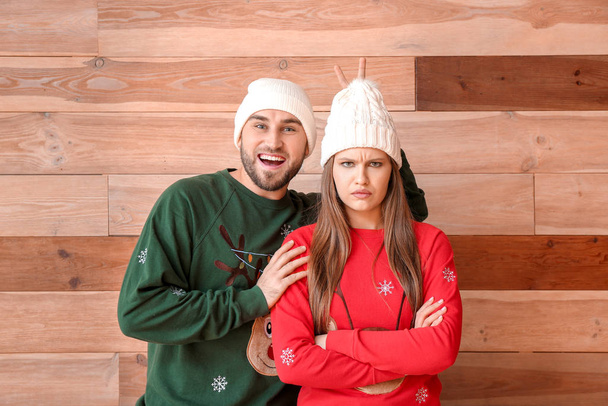 Portrait of emotional couple in Christmas clothes on wooden background - 写真・画像