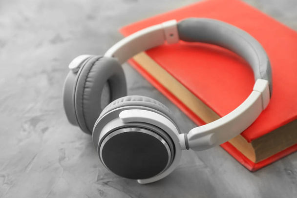 Buch und moderne Kopfhörer auf grauem Hintergrund. Hörbuchkonzept - Foto, Bild