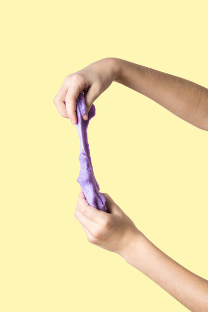 The child's hands stretch up a lilac slime on a yellow background. - Photo, Image